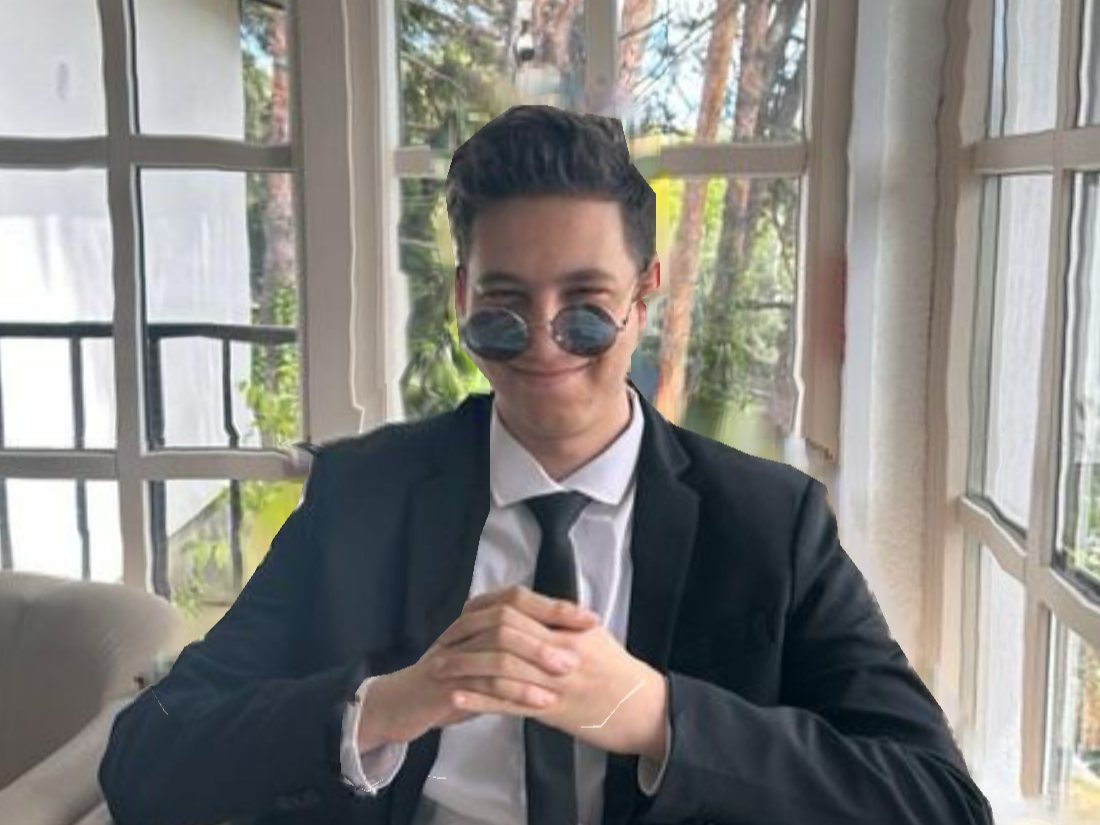 Alex in a black suit and round sunglasses, sitting by a sunny window