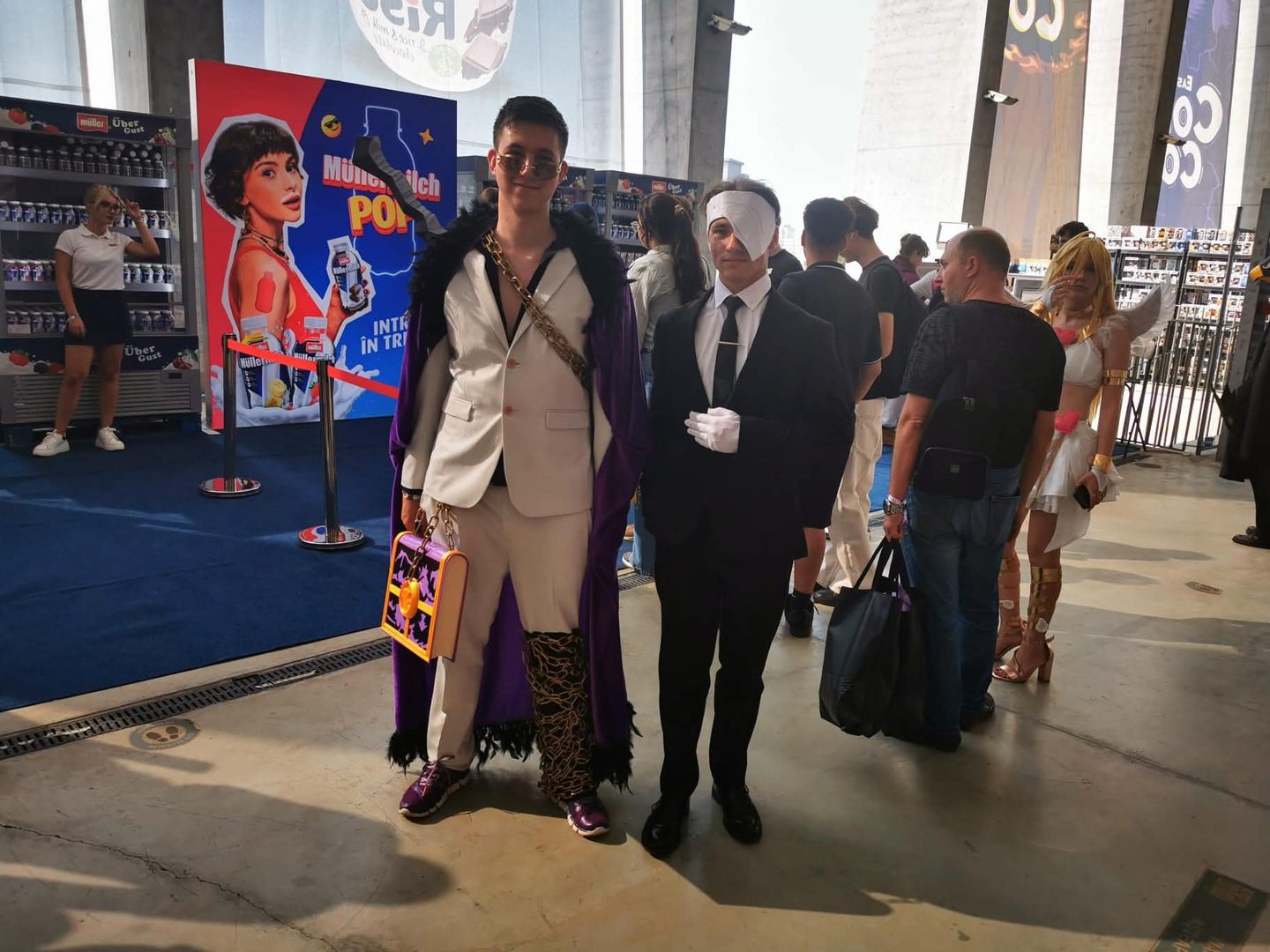 Alex in cosplay next to a cosplayer in a white mask, inside the convention hall