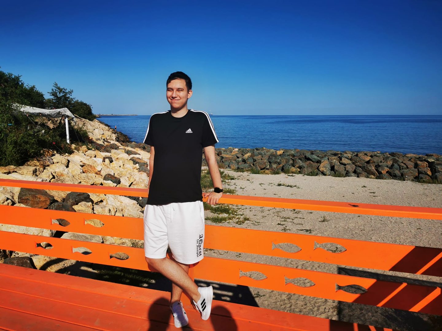 Alex leaning on an orange railing by the sea